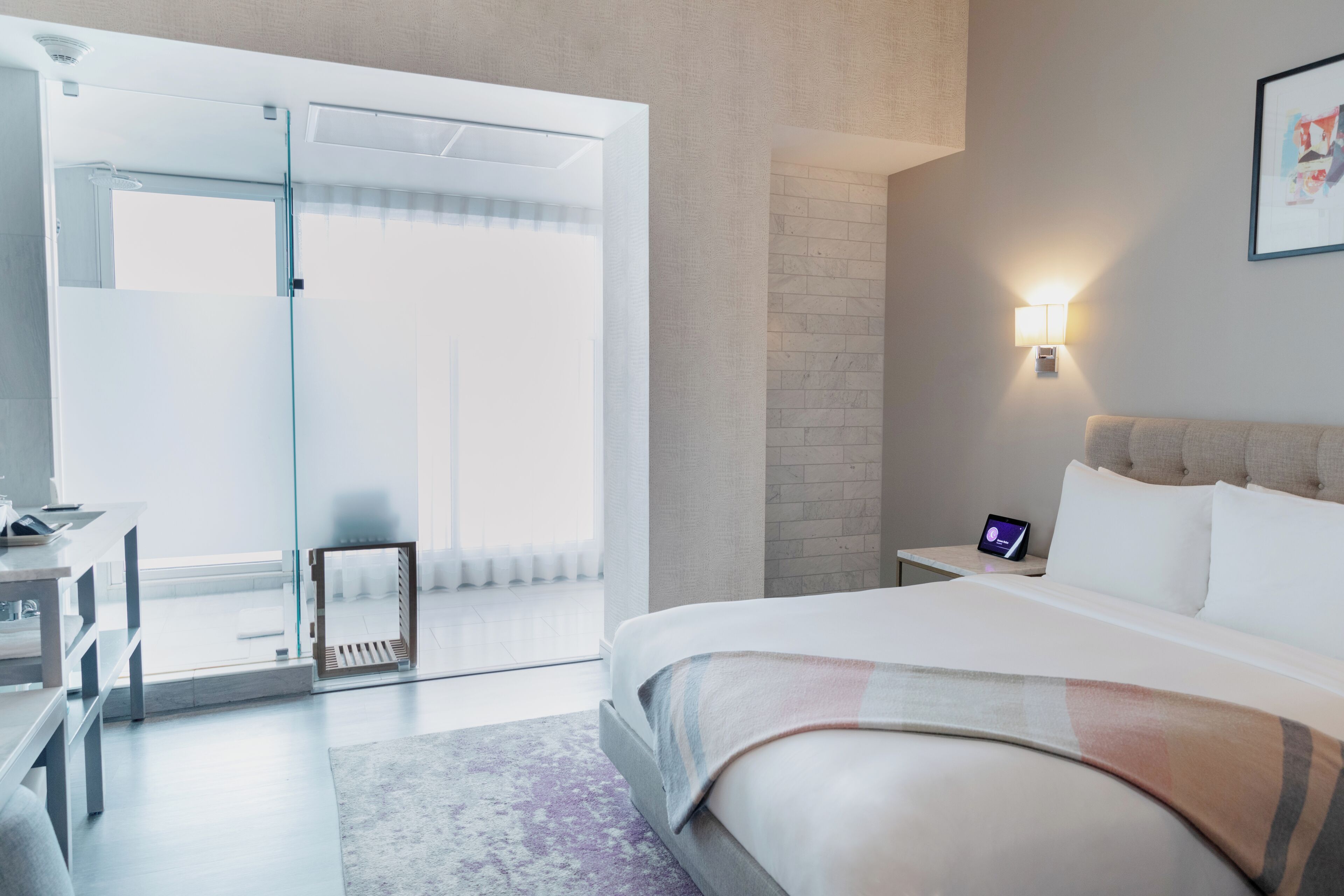 Una camera d'albergo moderna con un letto, un comodino e una porta vetrata che dà su un balcone.