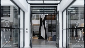 Moderne hotelentree met glazen deuren, een centraal zwart-wit decoratief paneel en metalen stoelen buiten.