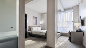 Een hotelkamer met een bed, nachtkastje, lamp en een groot raam.