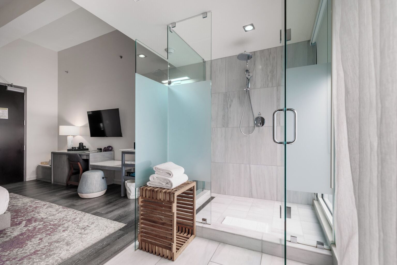 A modern bathroom with a glass shower enclosure, a vanity with a mirror, and a small seating area with a bench.