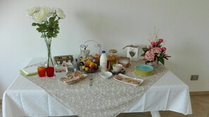 Une table à manger recouverte d’une nappe à motifs floraux, avec différents plats et un vase rempli de fleurs blanches.