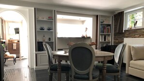 A dining area with a round table and chairs, a bookshelf, and a window with curtains. - Exclusive Flats Studio Swimming-pool (Dilbeek)