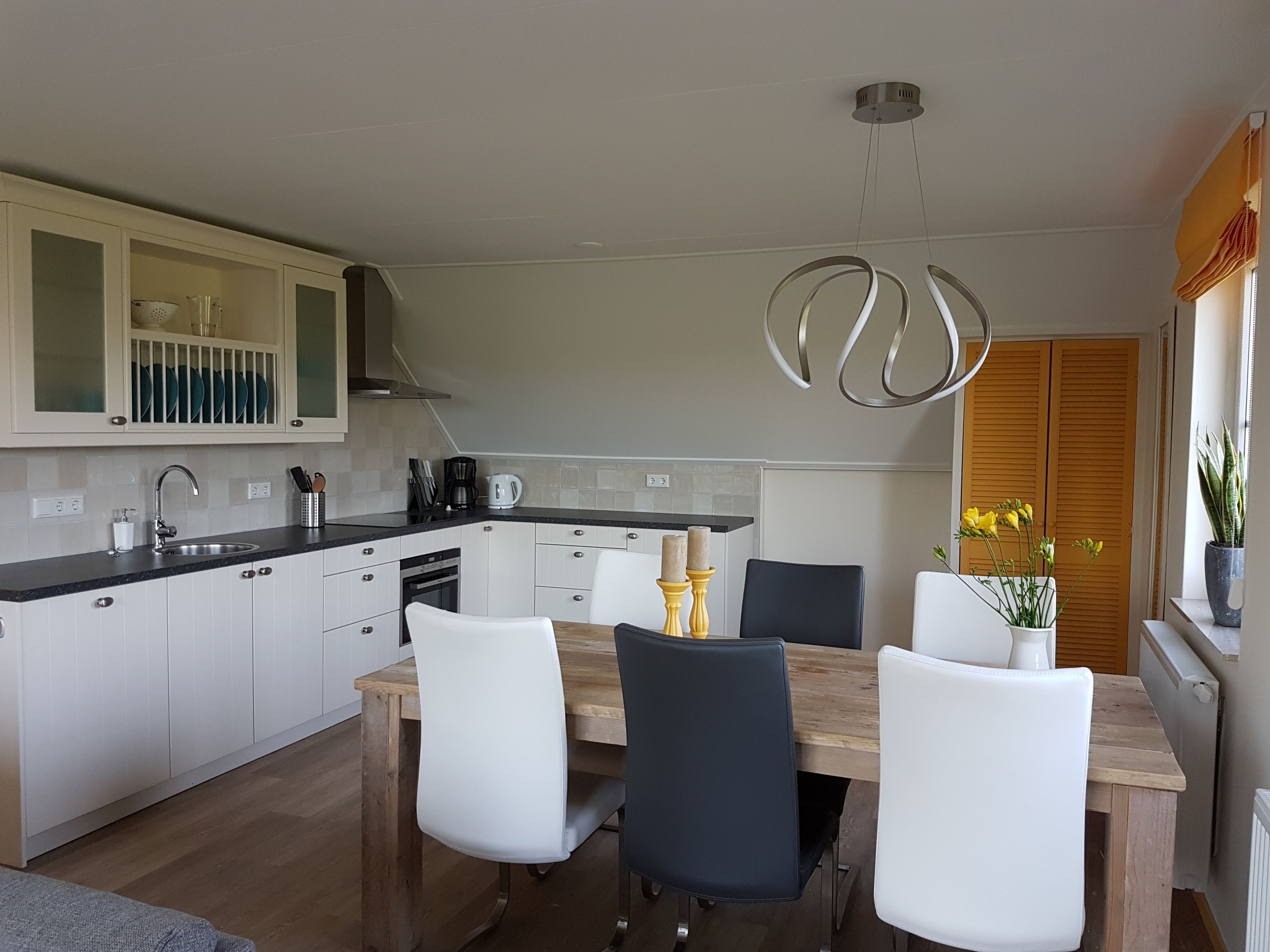 Une cuisine moderne avec des meubles blancs, une table à manger en bois et des chaises noires.