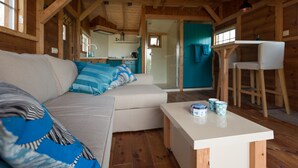A cozy log cabin interior with a sofa, a small table, and a kitchen area visible through an open door. - Aan de Waterspiegel (Aagtekerke)