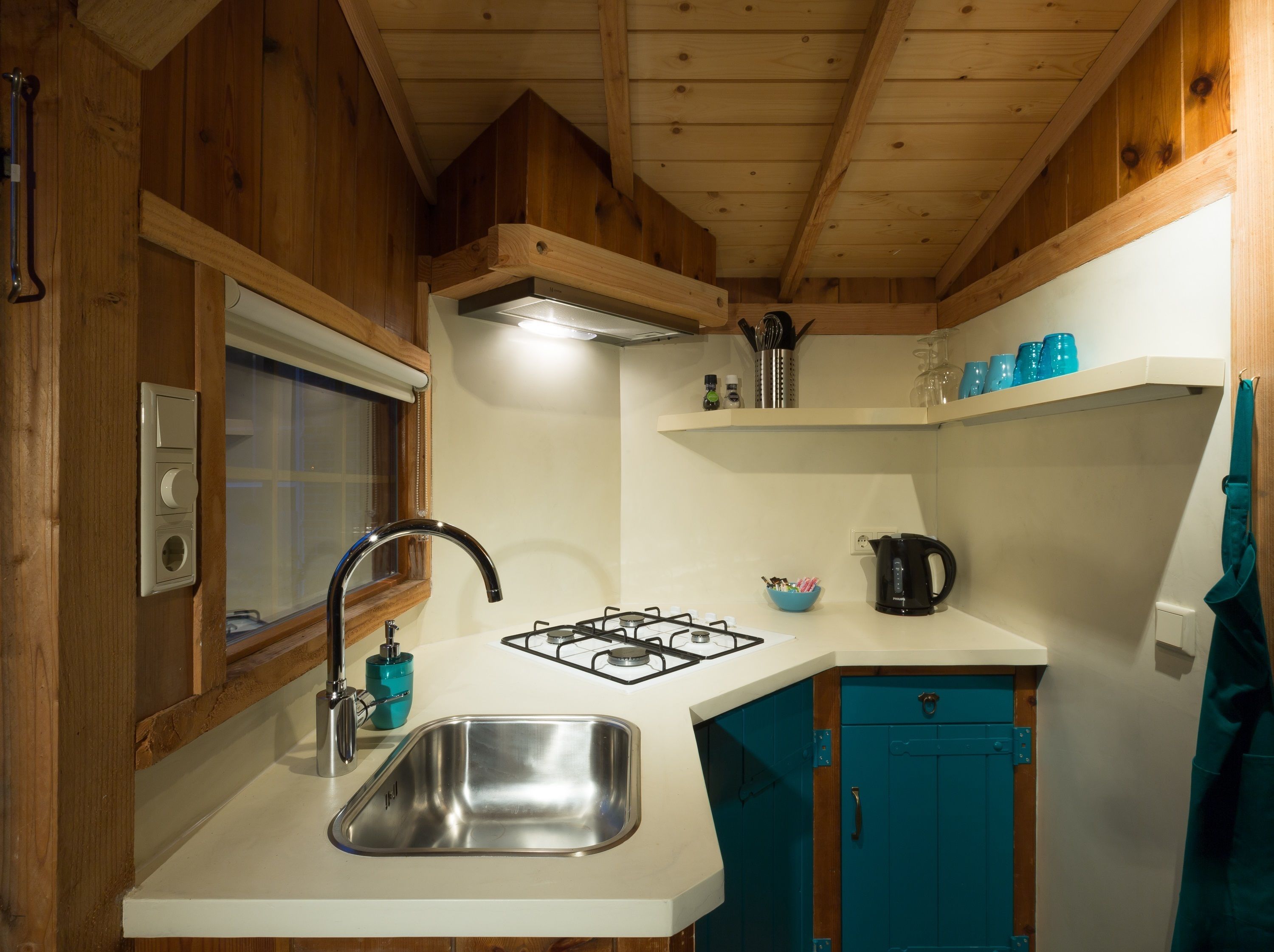 Una cocina compacta con lavamanos, grifo, estufa y armarios color turquesa.