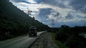 A rural road with a vehicle, surrounded by greenery and power lines.