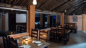 A restaurant with wooden tables and chairs, a high ceiling with exposed beams, and a large window overlooking the street.