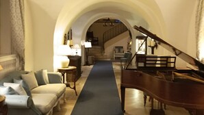 A grand piano, a sofa, and a hallway with an arched ceiling. - Hôtellerie du Château de Floure & Spa (Floure)