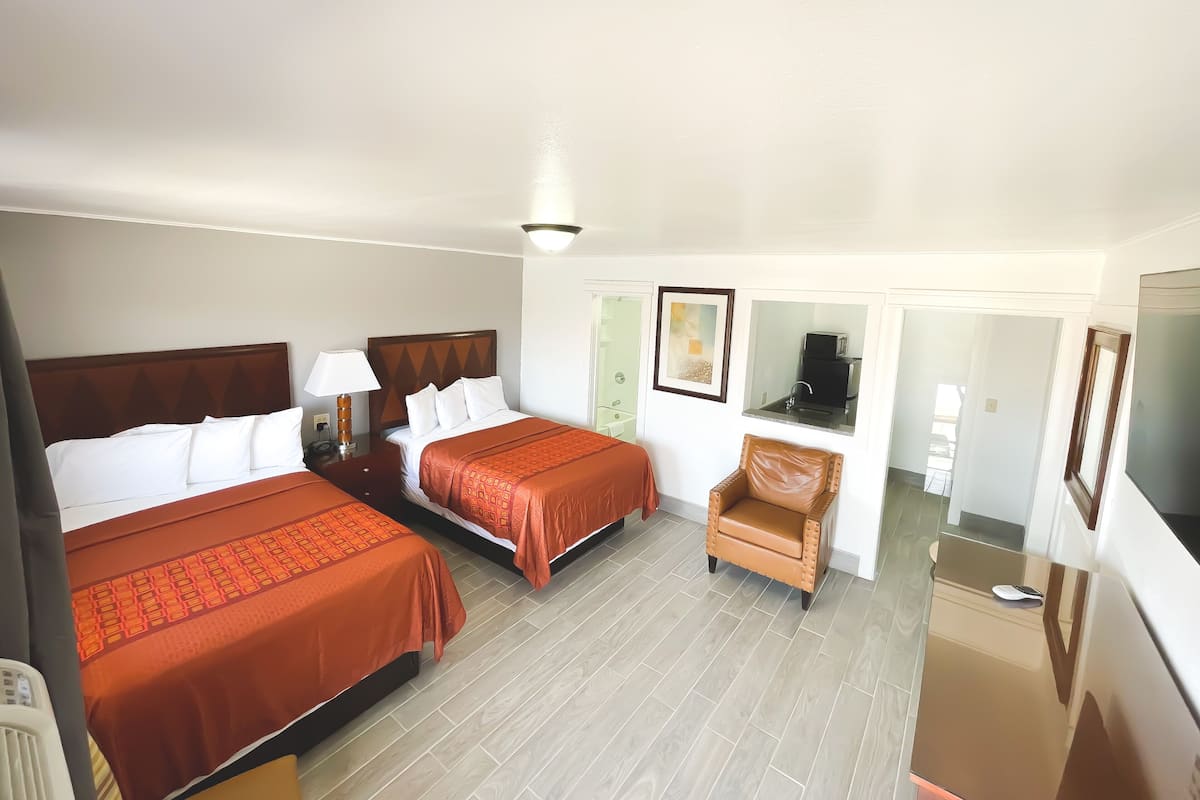 A hotel room with two beds, a chair, a desk, a TV, and a bathroom visible through a door.