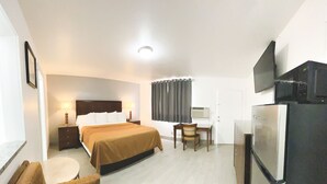 A hotel room with a bed, a desk, a chair, a sofa, a television, and a refrigerator.