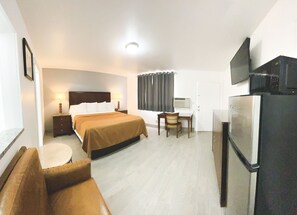 A hotel room with a bed, a desk, a chair, a sofa, a television, and a refrigerator.