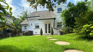 Une maison avec une pelouse bien entretenue, des dalles de pierre servant de chemin et un espace barbecue.