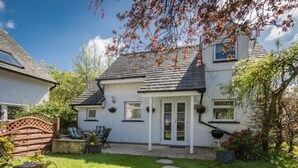 Une maison à deux étages, avec une façade blanche, un toit foncé et une porte d’entrée dotée de panneaux de verre. On y trouve un patio avec un barbecue et des meubles d’extérieur.