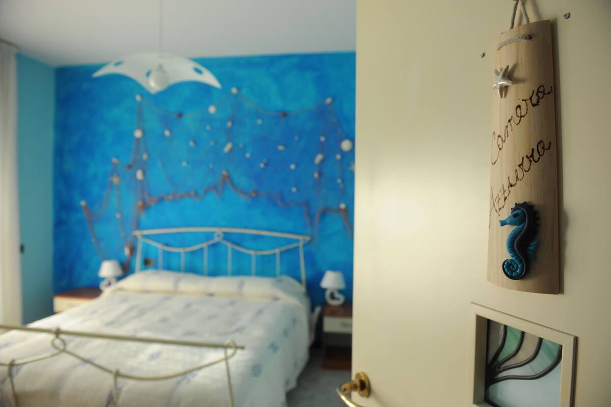 Een slaapkamer met een blauwe wand, een bed met metalen frame, een houten hoofdbord en een wanddecoratie.