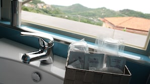 Ein Badezimmer mit Waschbecken, Wasserhahn und einem Fenster mit Blick auf eine Stadt und Hügel.