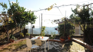 Eine Terrasse im Freien mit Tisch und Stühlen, umgeben von Blumentöpfen und einem Pflasterboden.