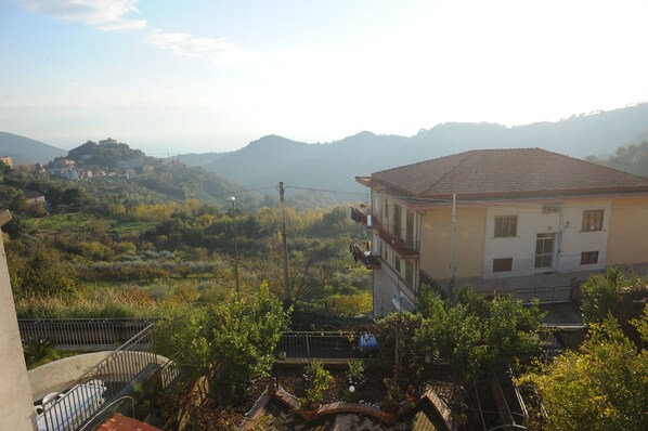 A building with a tiled roof, surrounded by greenery and hills in the background. - B&B Viale delle Colline (Salerno)