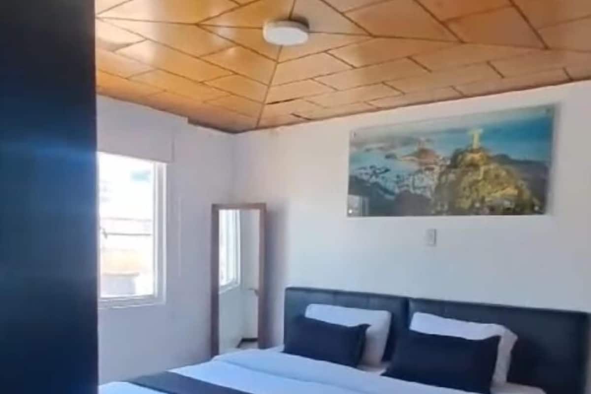A bedroom with a bed, a painting on the wall, and a window.