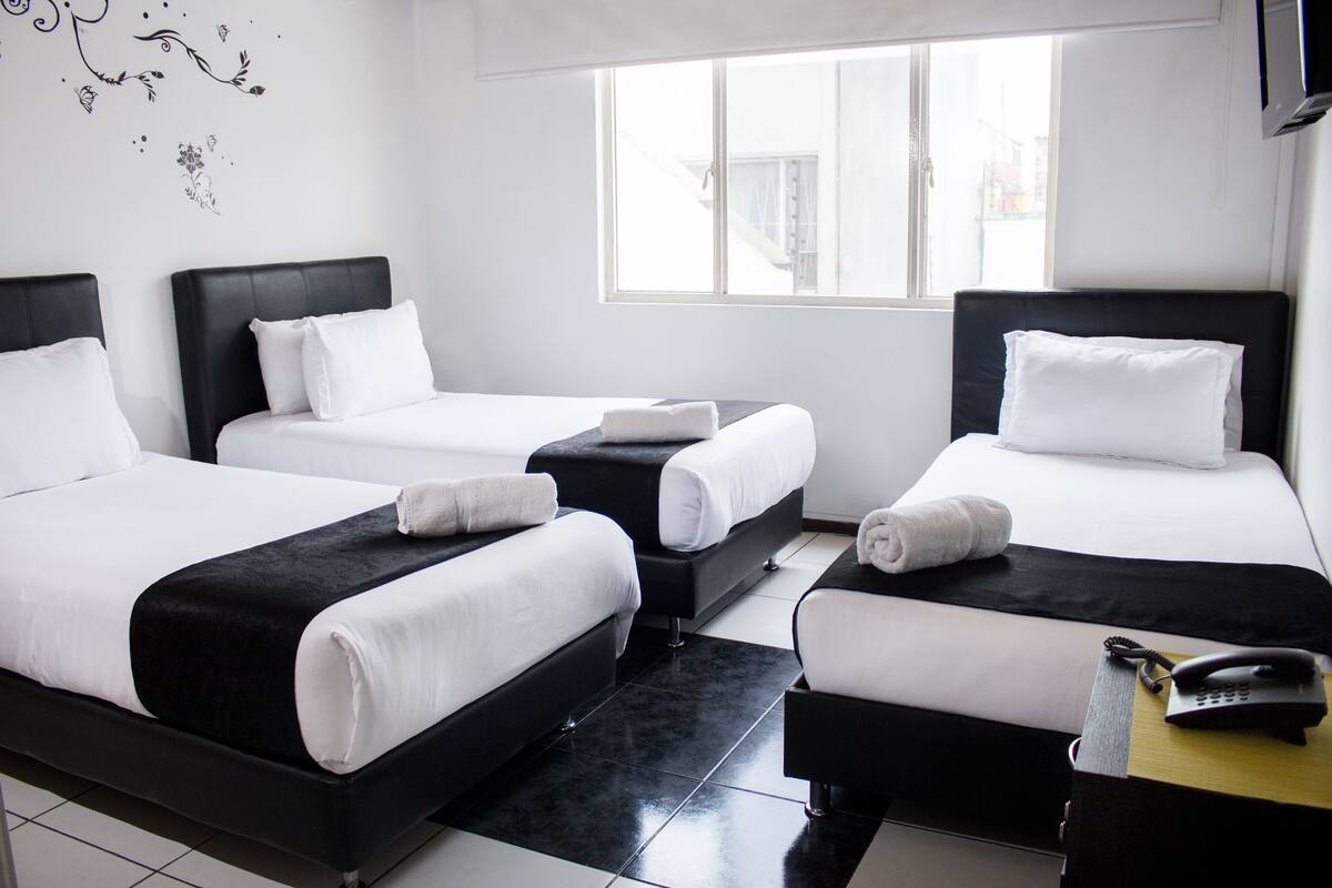 A hotel room with three beds, a black and white color scheme, and a window providing natural light.