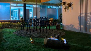 An outdoor patio with a table and chairs, a fire pit, and hanging plants. - Hotel Normandia Gold (Bogotá)