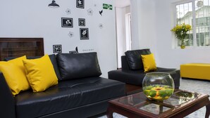 A modern living room with black leather sofas, yellow cushions, and a glass coffee table. - Hotel Normandia Gold (Bogotá)