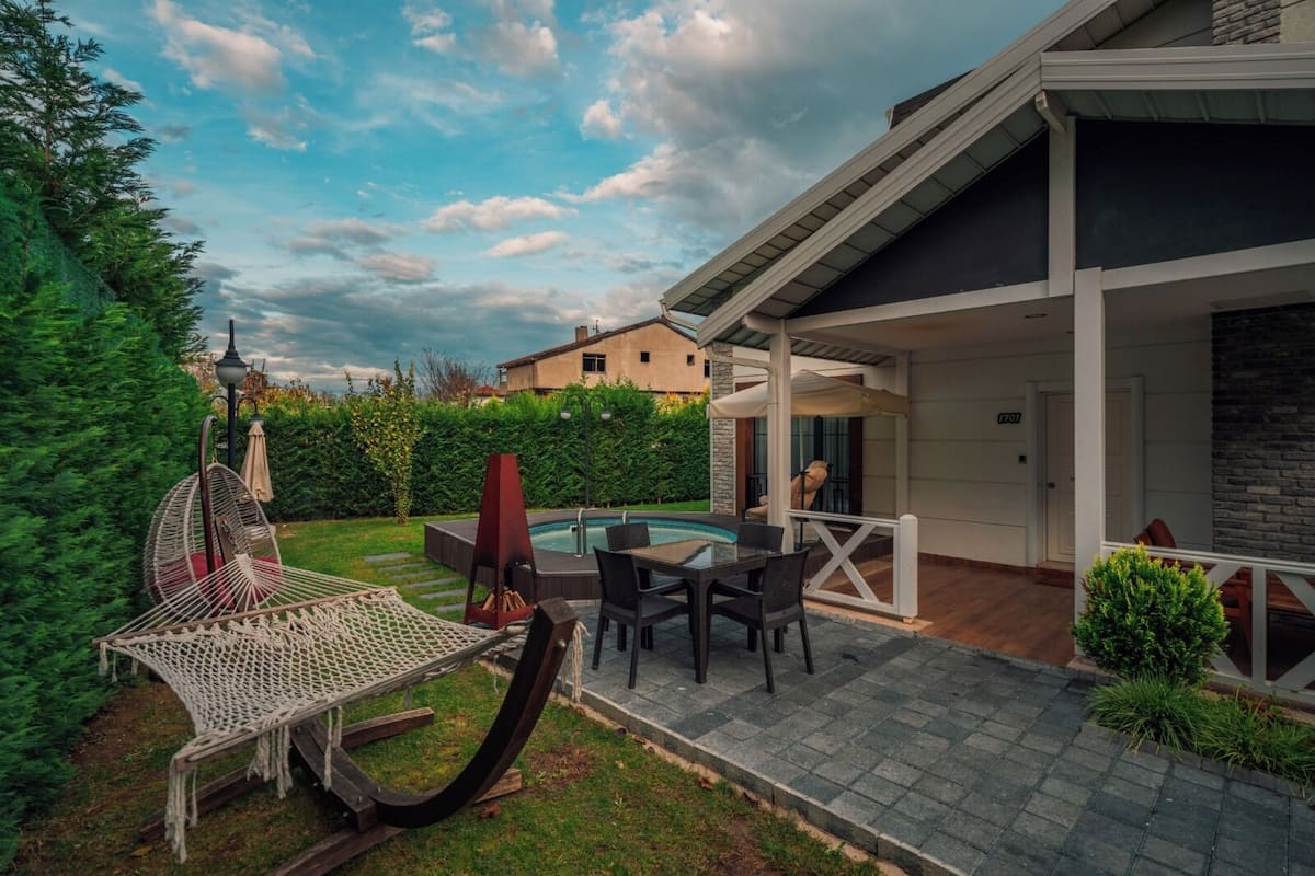 Un patio moderno al aire libre con una mesa y sillas de vidrio, un jacuzzi y una hamaca.