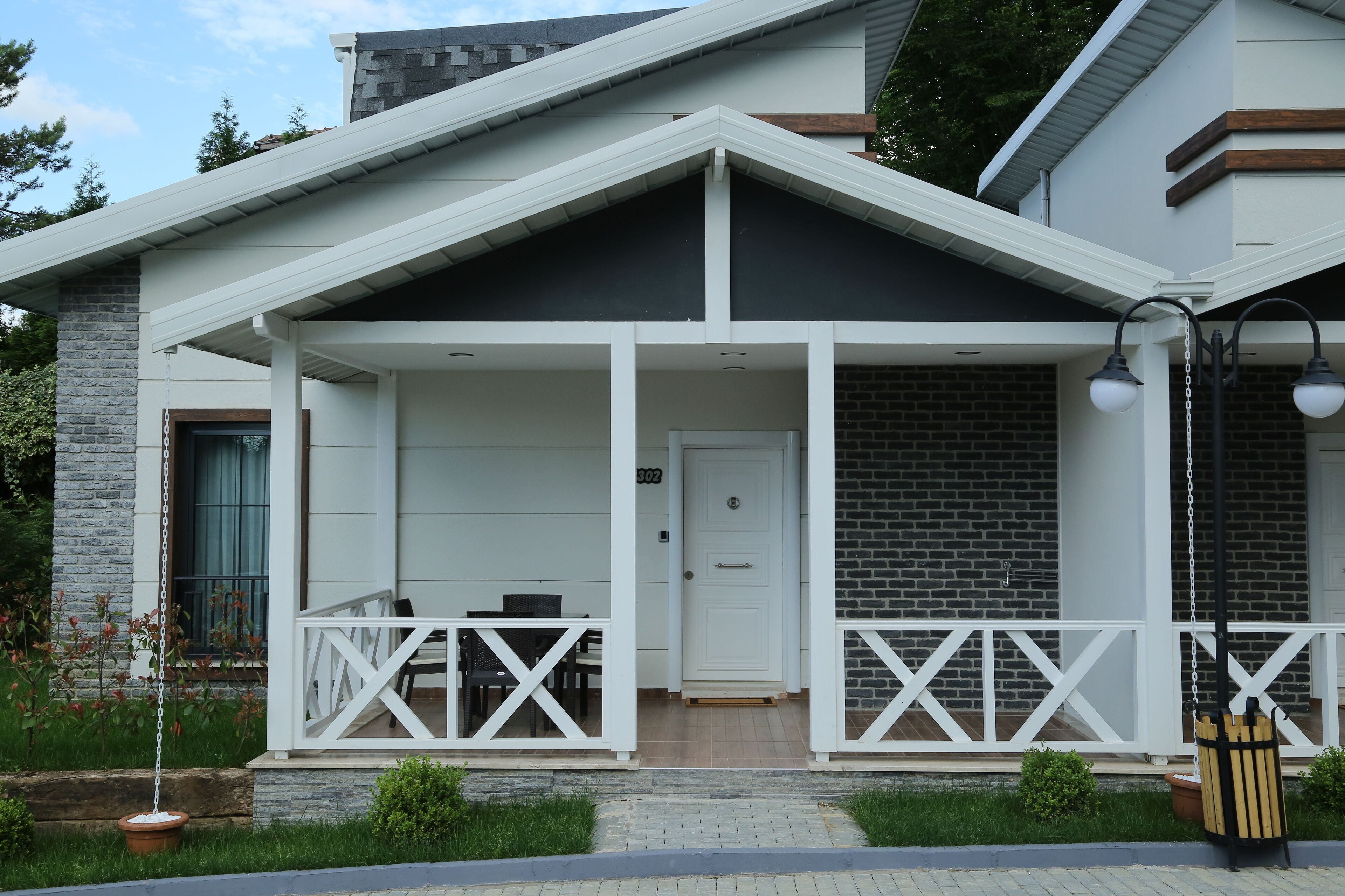 Ein modernes Haus mit überdachter Veranda, einer Tür und einem kleinen Garten.