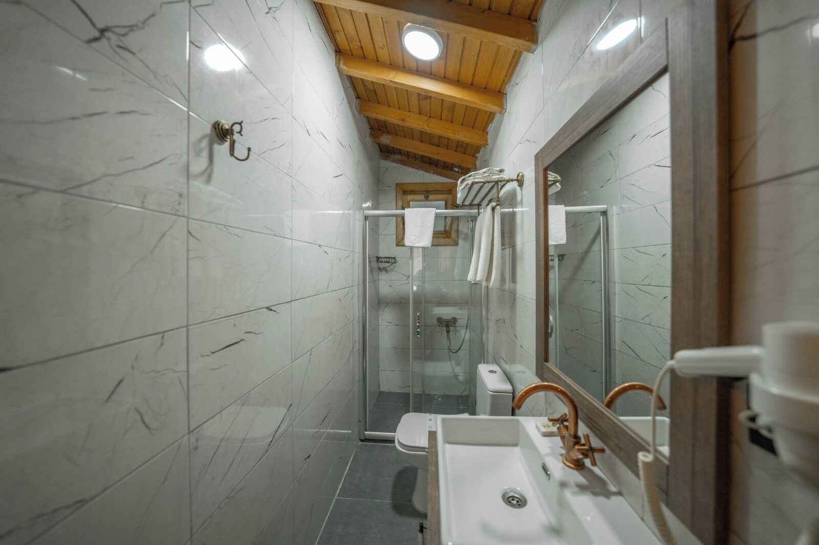 A bathroom with marble walls, a wooden ceiling, a glass shower enclosure, and a sink with a mirror.
