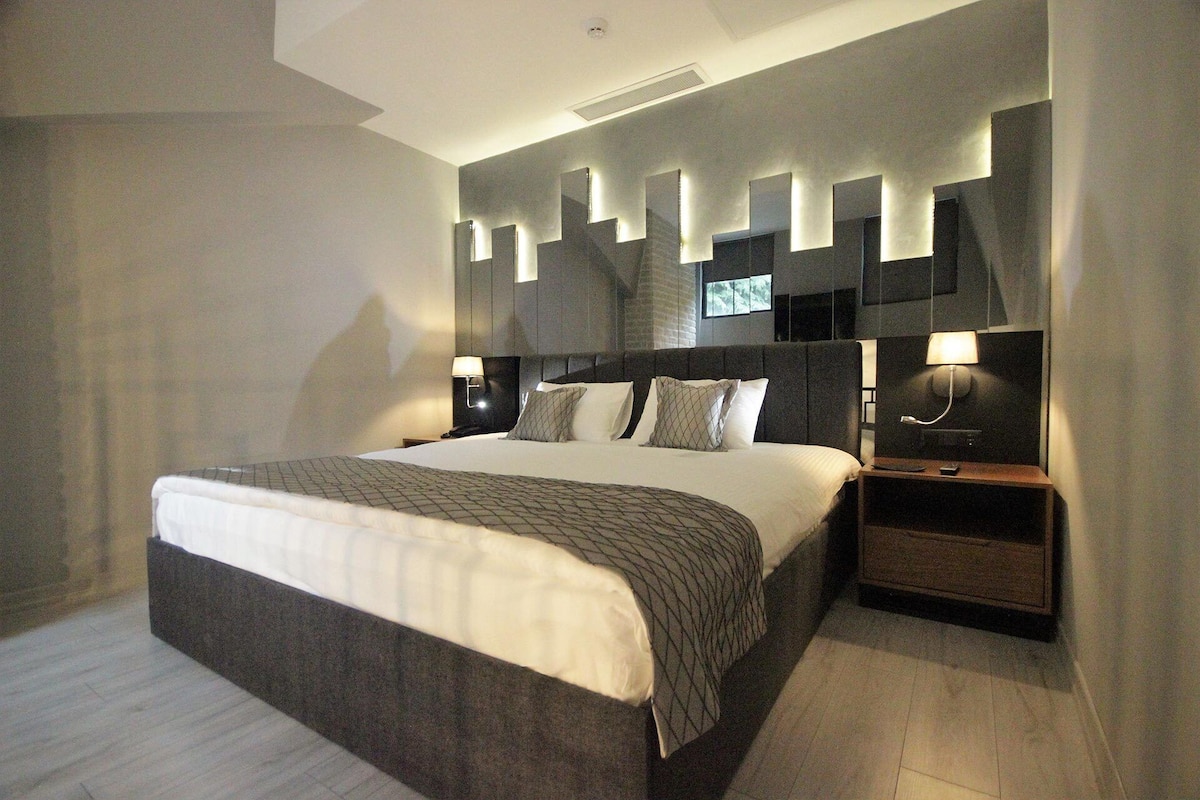 Un dormitorio moderno con una cama grande, dos mesitas de noche y una lámpara fijada a la pared.