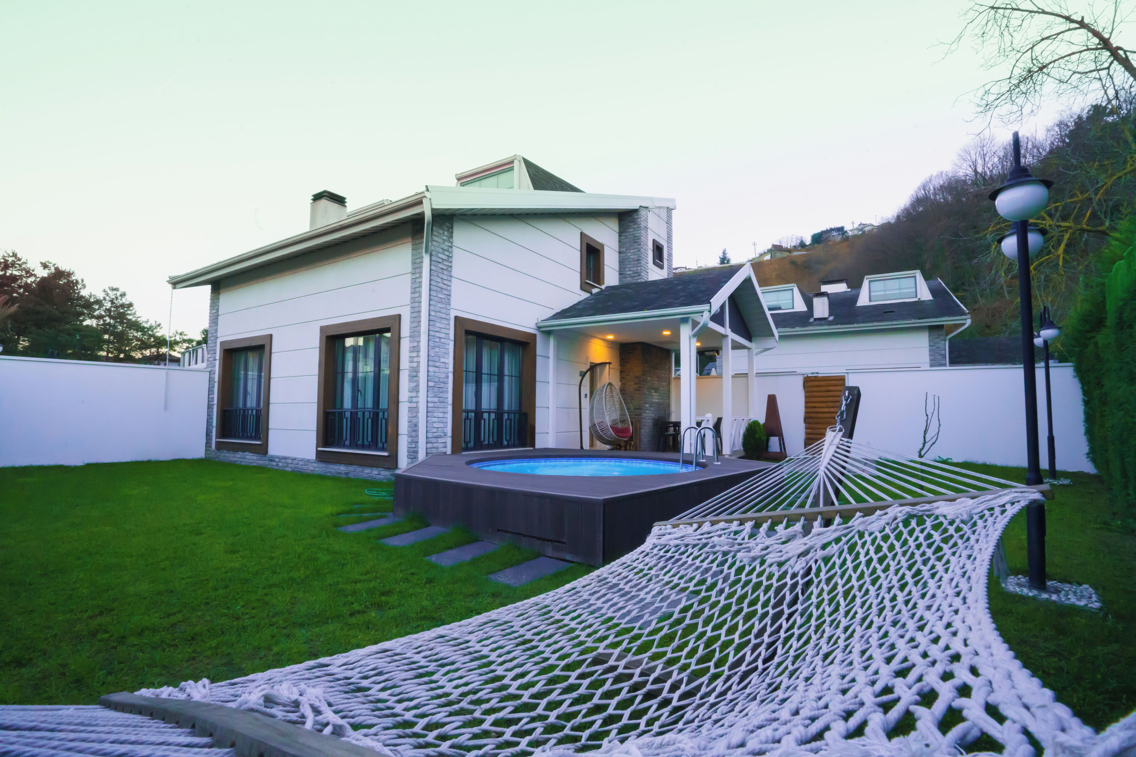 A modern house with a swimming pool, a hammock, and a well-maintained lawn.