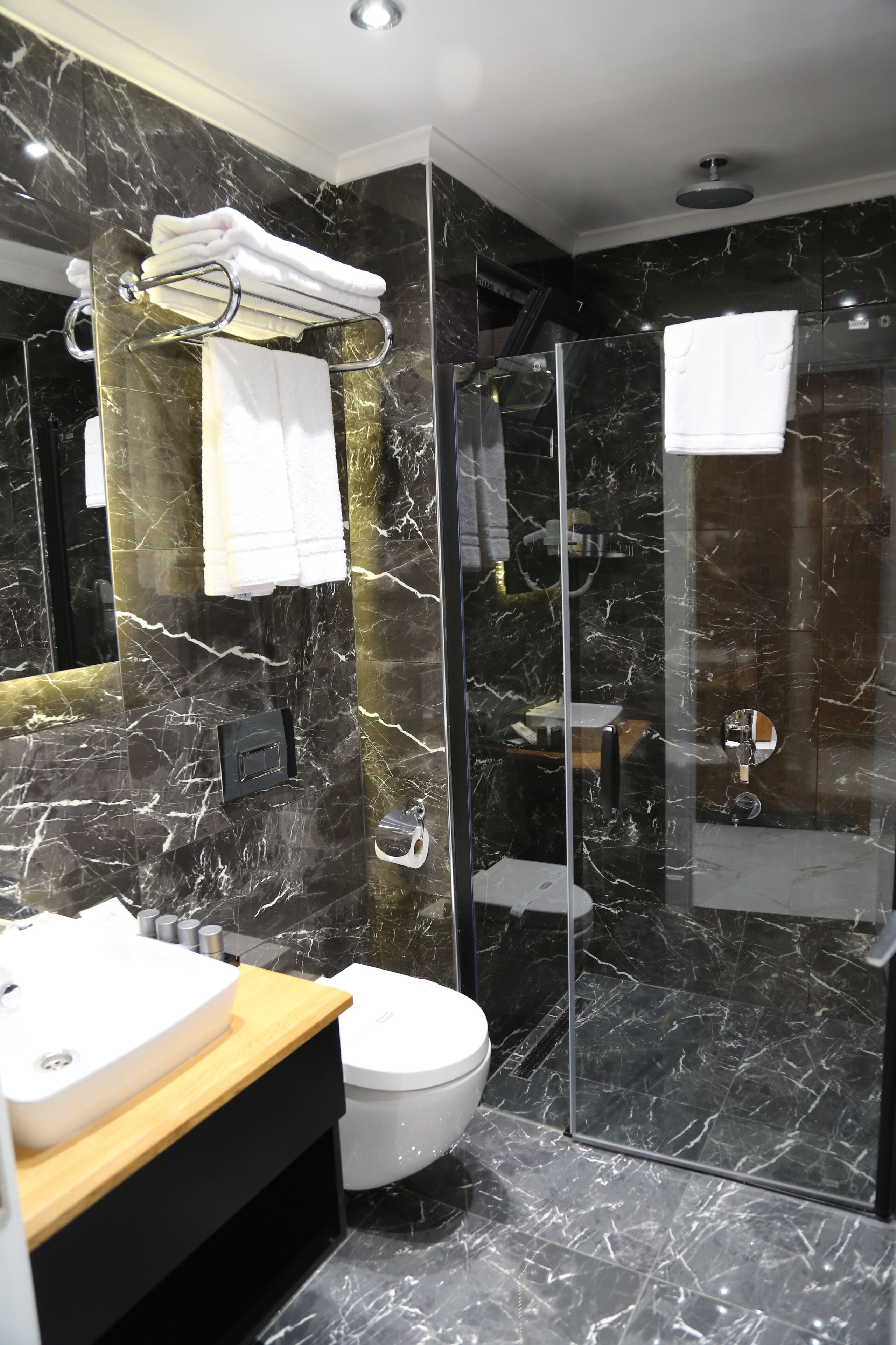 A modern bathroom with a marble wall, a glass shower enclosure, a white sink, and a toilet.