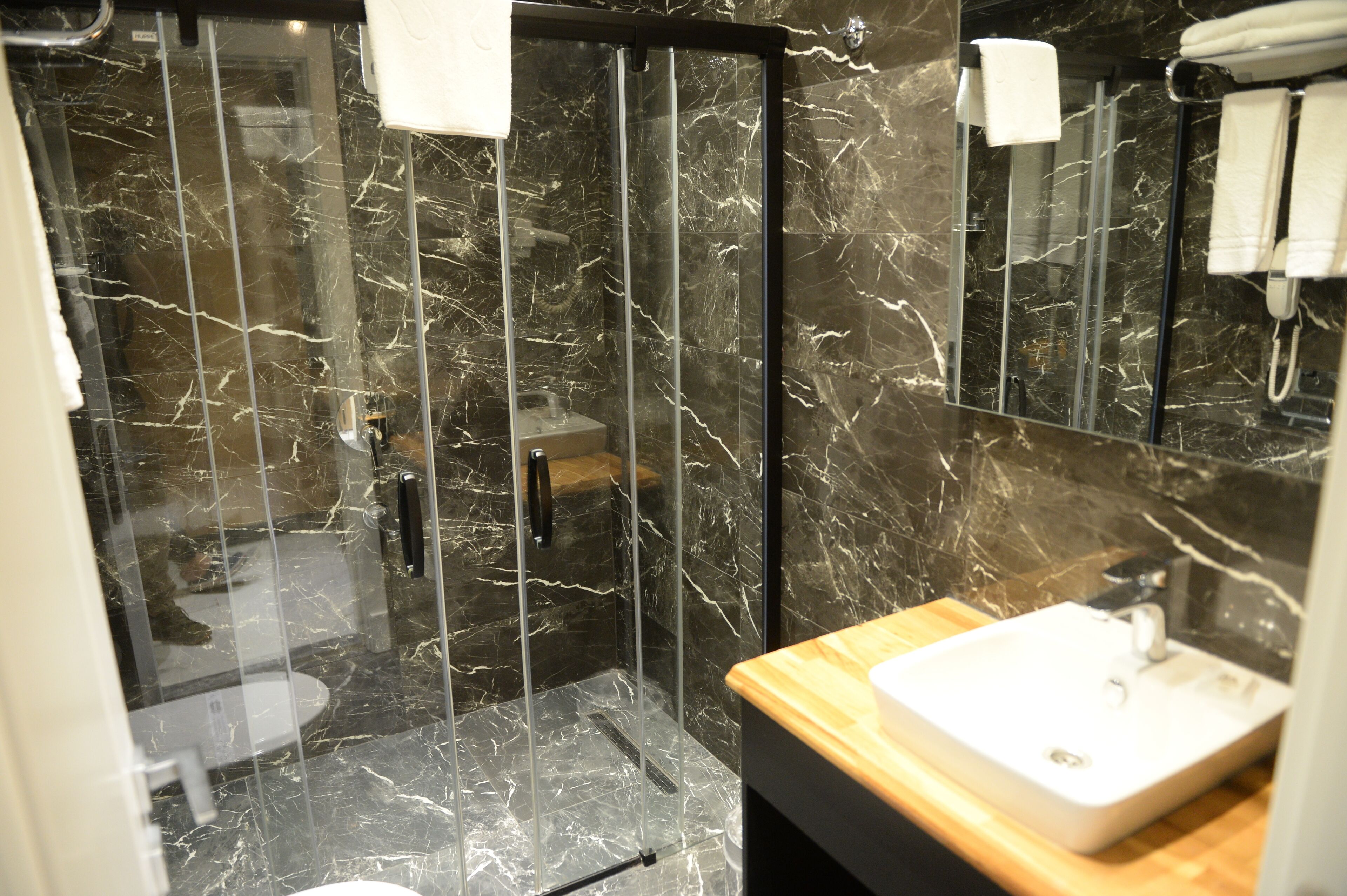 A modern bathroom with a glass-enclosed shower, a marble-tiled floor, and a wooden vanity with a sink.