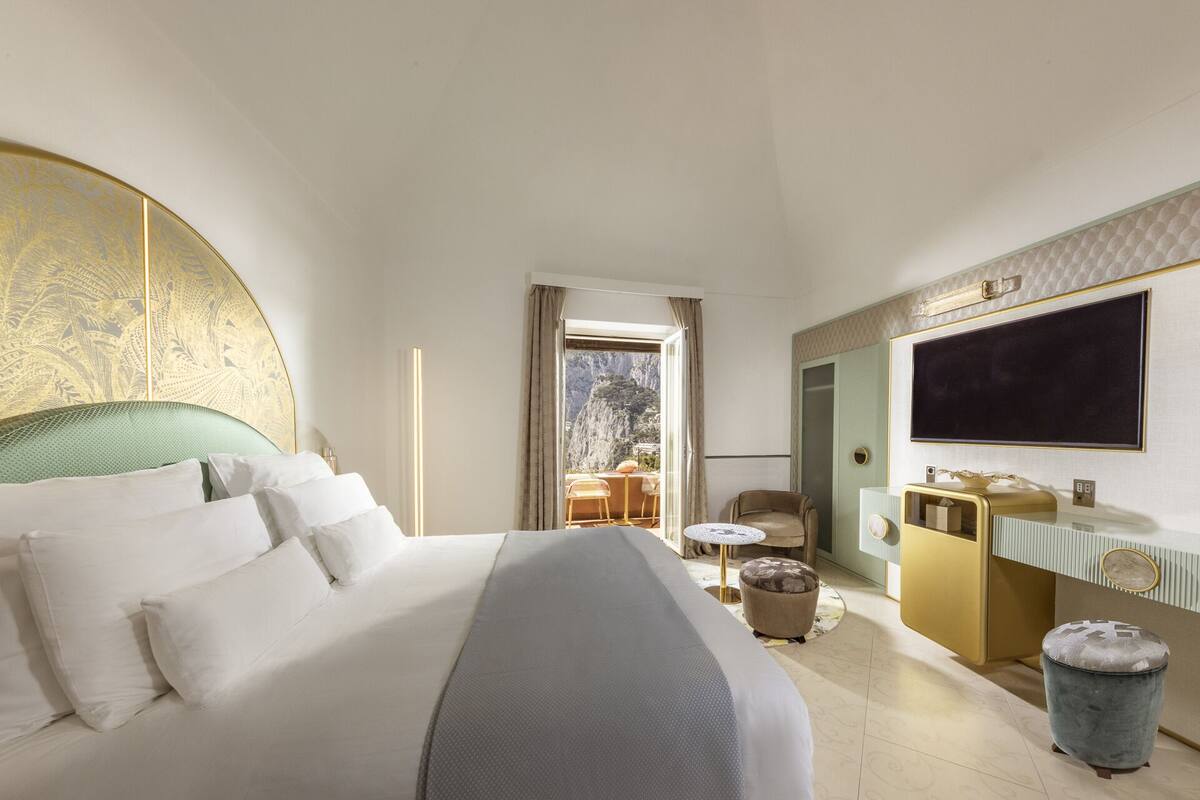A hotel room with a large bed, a desk, a chair, a TV, and a view of a mountain.