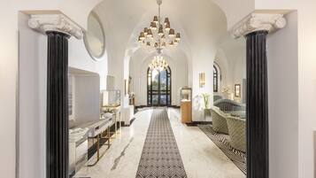 Un'imponente sala con tappeto decorato, colonne classiche, un lampadario e una zona salotto con cuscini fantasiosi.