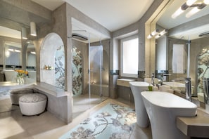 A modern bathroom with a large mirror, two sinks, a shower, and a decorative rug.