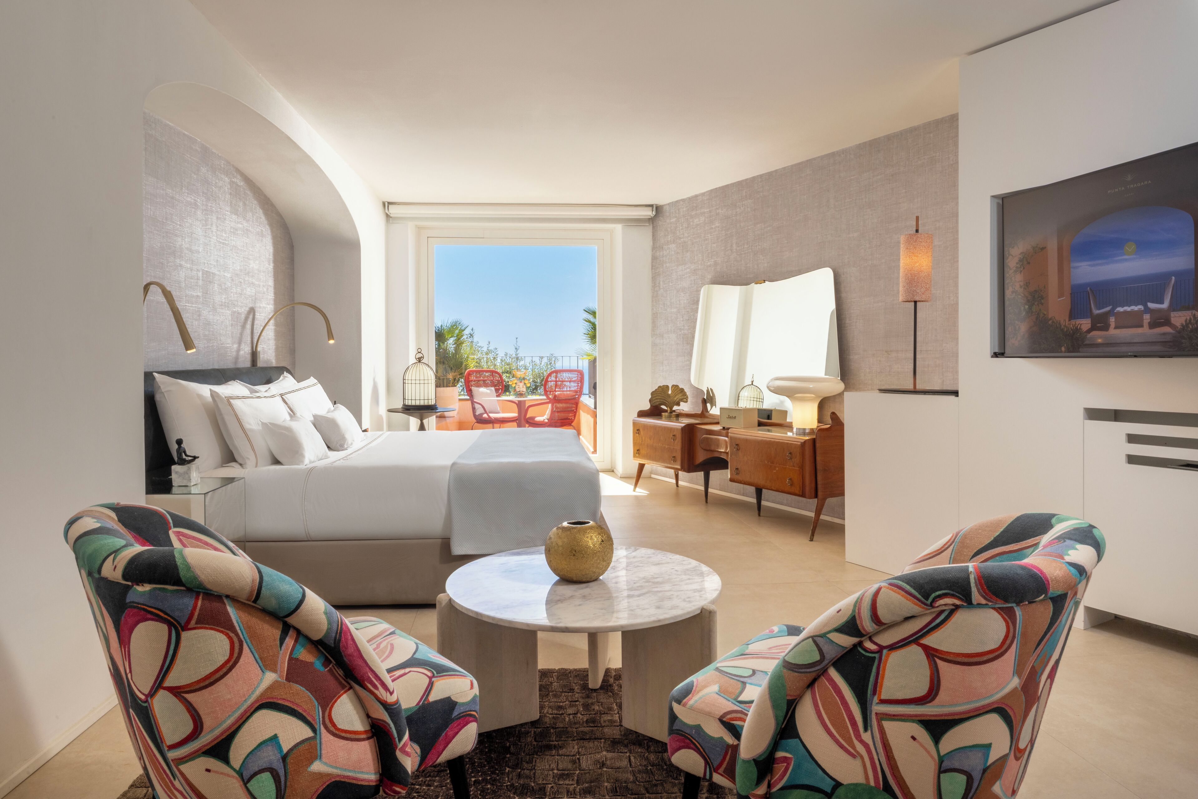 A hotel room with a bed, a desk, two chairs, a round table, and a view of the outdoors.