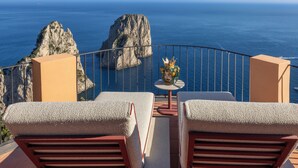 A balcony with two chairs and a small table, overlooking a rocky coastline and the sea. - Hotel Punta Tragara (Capri)