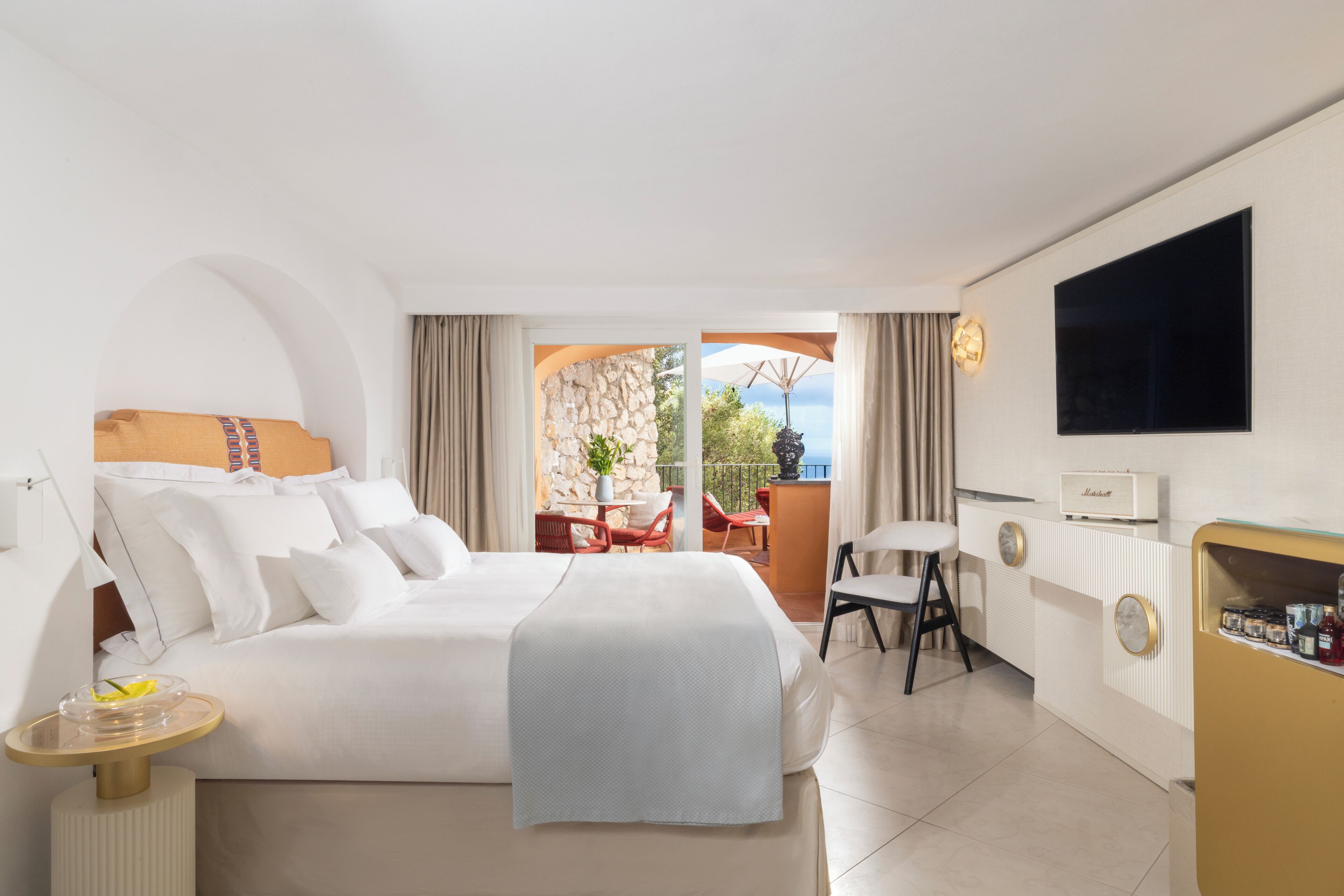 A hotel room with a large bed, a desk, a chair, a TV, and a balcony with a view.