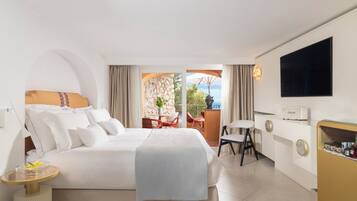 A hotel room with a large bed, a desk, a chair, a TV, and a balcony with a view.
