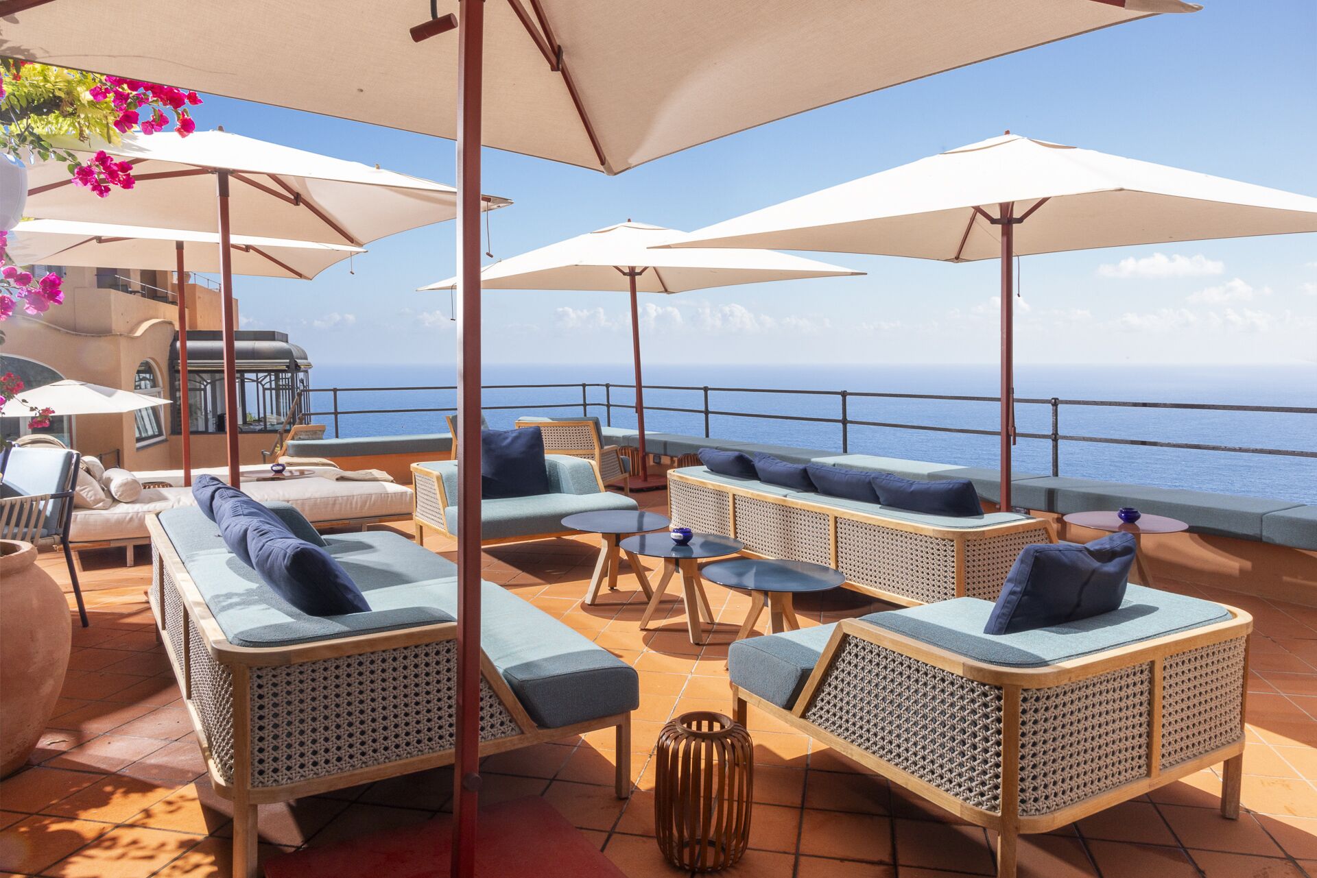 A sunlit outdoor seating area with wicker furniture and white umbrellas, overlooking the sea.