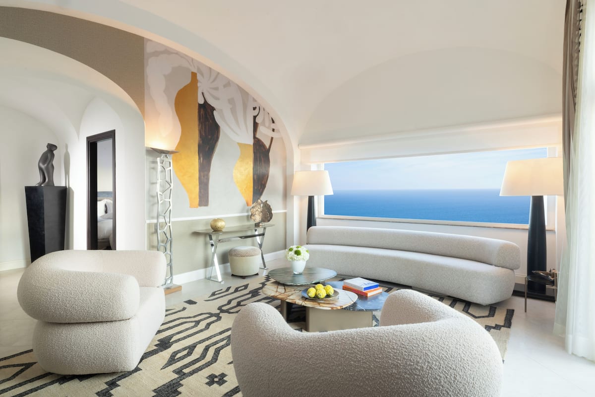 A modern hotel room with a sofa, armchairs, a coffee table, and a view of the sea.