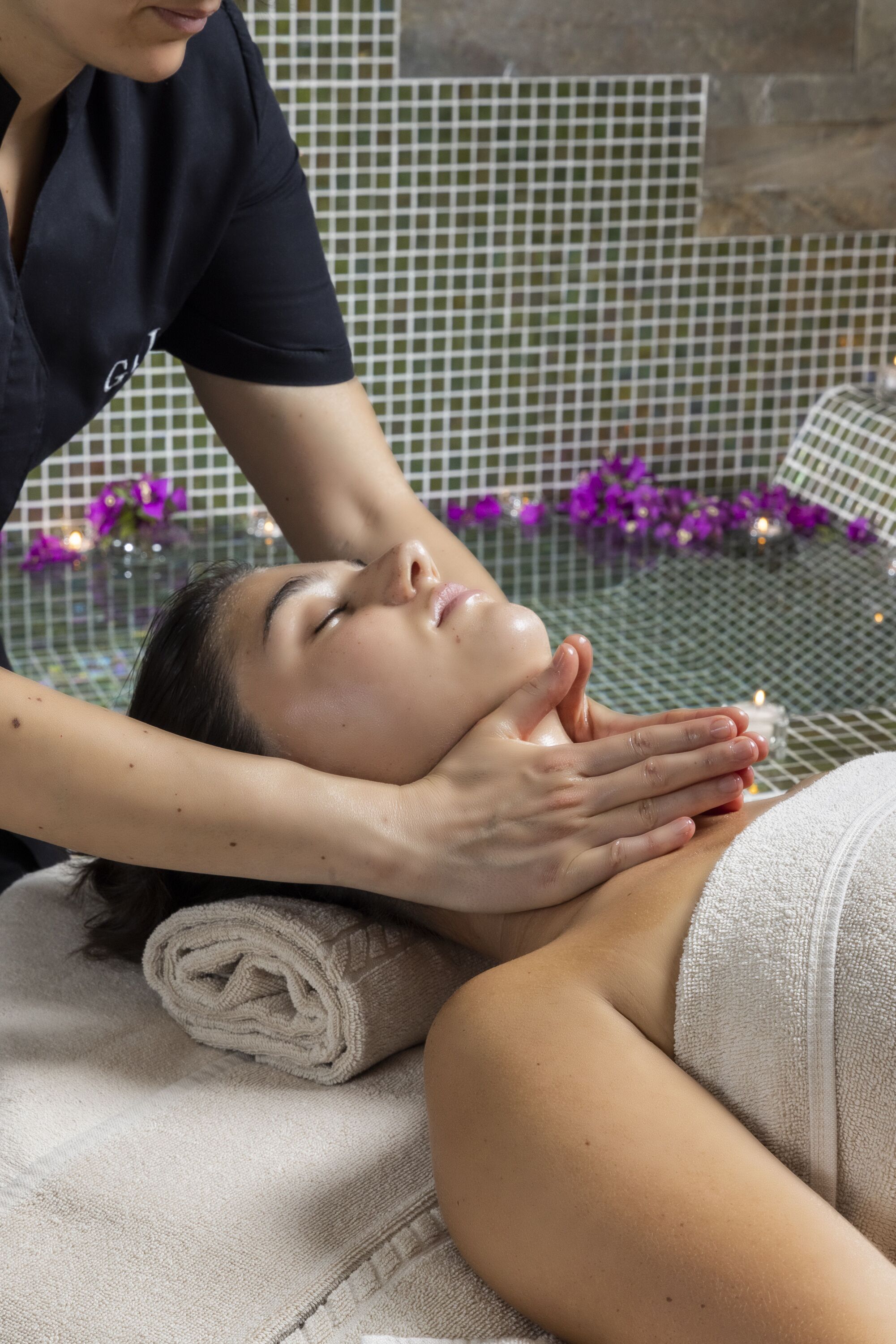 Eine Person erhält eine Massage in einem Raum mit Fliesenwand und Glastisch.