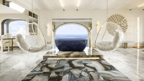 A modern interior with a large view of the ocean through an arched doorway, two hanging chairs, and a unique decorative wall piece. - Hotel Punta Tragara (Capri)