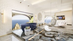 A modern interior with a large window overlooking the sea, a marble floor, and a seating area with a hanging chair and a sofa. - Hotel Punta Tragara (Capri)
