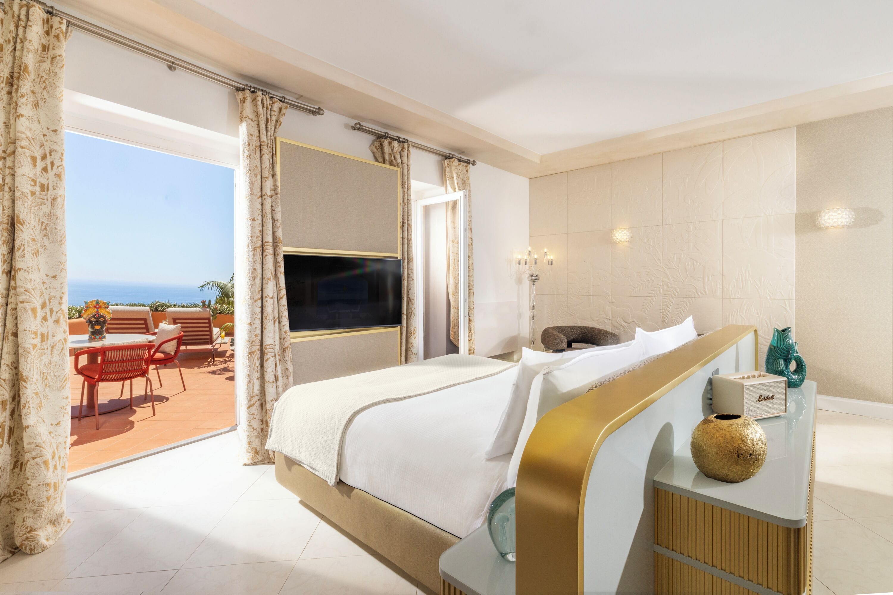 Habitación de hotel con cama, televisor, mesita de noche con un florero y vistas al exterior.