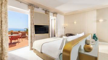 Habitación de hotel con cama, televisor, mesita de noche con un florero y vistas al exterior.