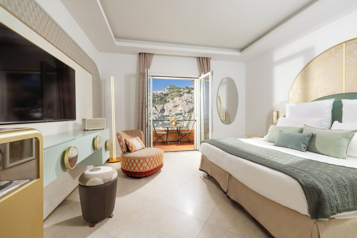A modern hotel room with a bed, a TV, a small table, and a view of a balcony.