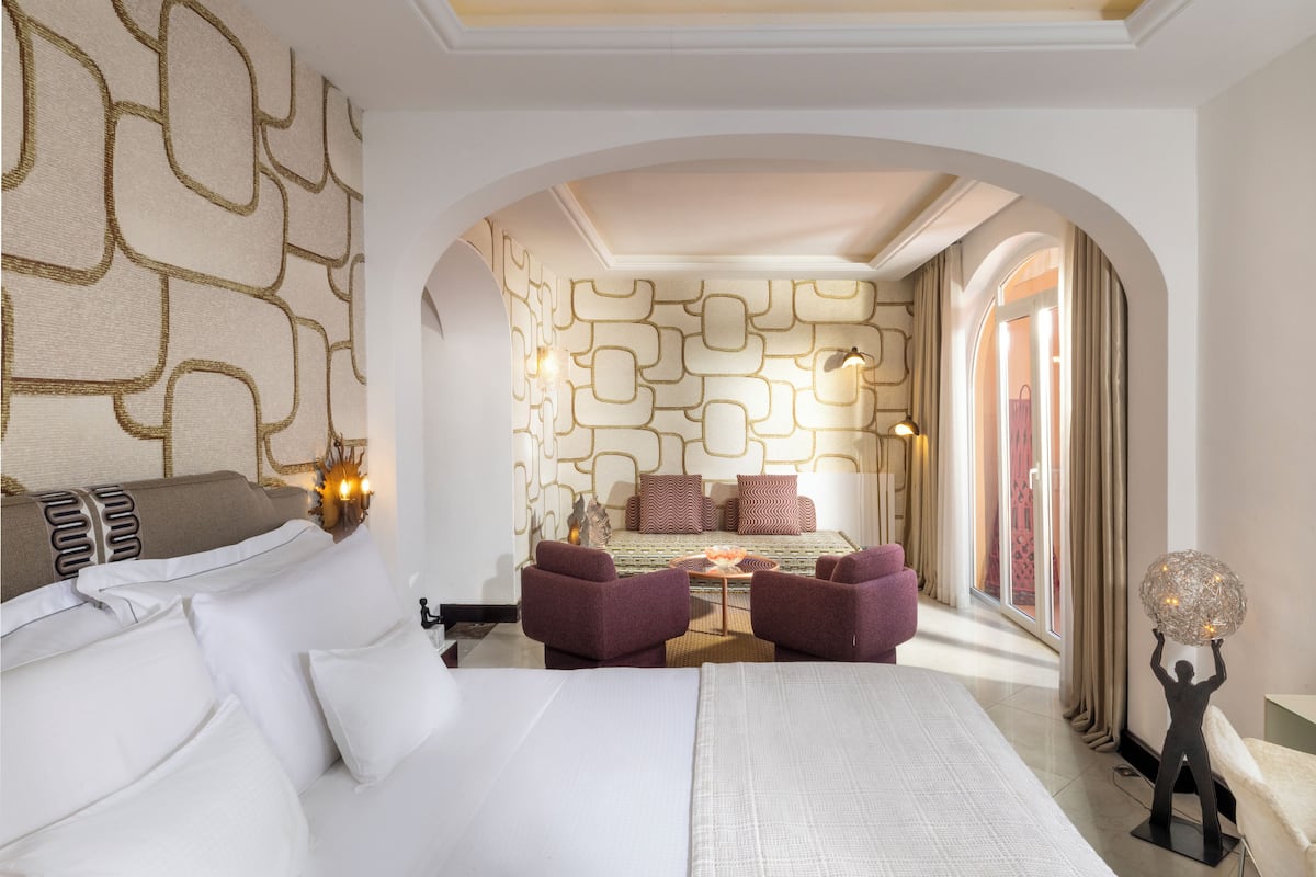 A hotel room with a large bed, two armchairs, a small table, and a decorative light fixture.