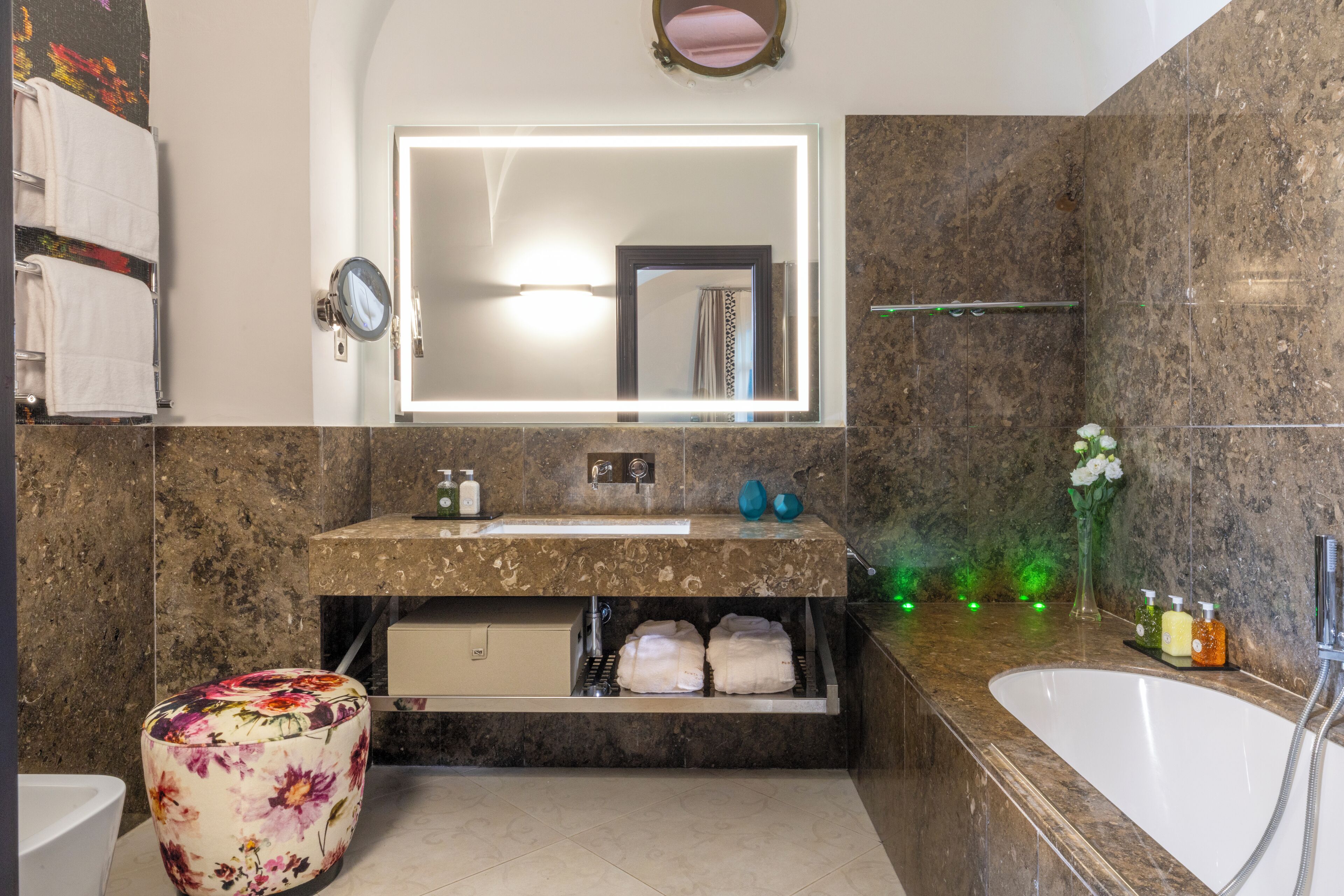 Un baño con lavamanos de mármol, un espejo grande, una bañera y un reposapiés floral.
