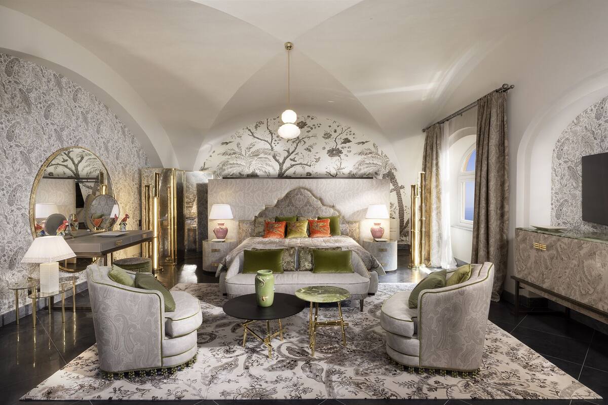 A luxurious bedroom with a large bed, two armchairs, a round coffee table, and a television.
